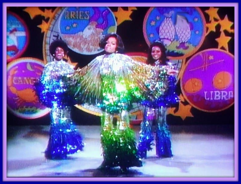 Diana Ross and the Supremes performing onstage in brightly colored outfits and psychedelic circles on the backdrop behind them