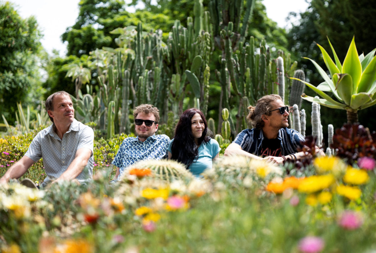 Juleah and her band sitting in park with yellow, orange, and pink flowers in green grass with green trees behind them