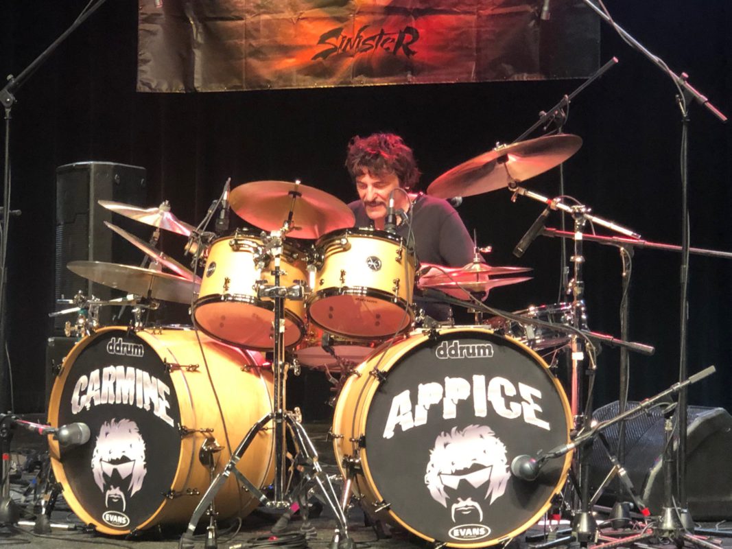 Carmine Appice peforming behind his massive, twin bass drum kit with his last name and facial image on each bass drum