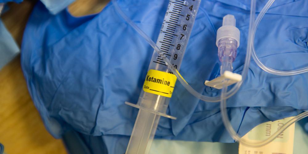 ketamine syringe laying on top of blue medical scrubs