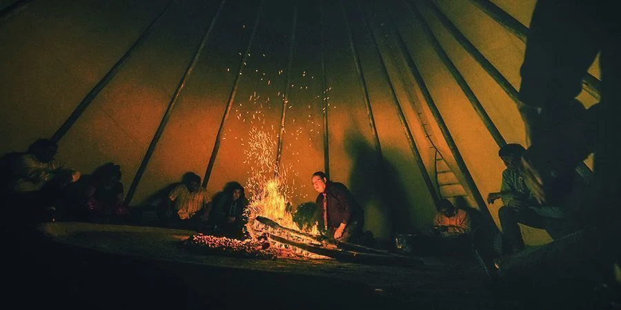 Photo taken inside a teepee with people sitting in a circle around a fire participating in a peyote ritual