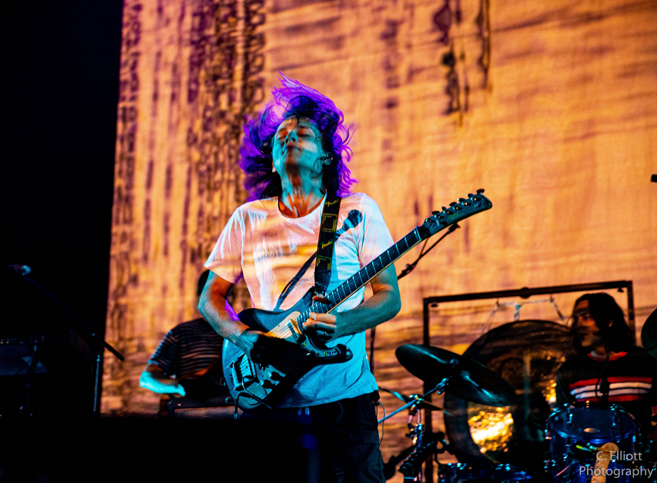 King Gizzard and the Lizard Wizard's guitarist playing wildly with hair flying and looking purple due to lighting