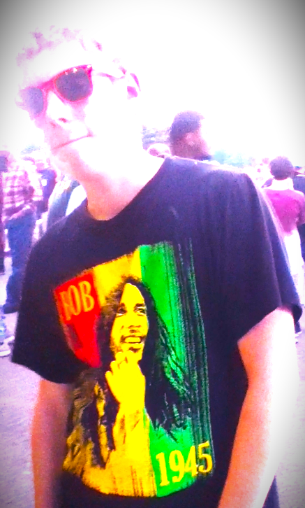 Slater, a young white man with blond hair wearing red sun glasses a black shirt with a bright red, green, and yellow image of Bob Marley on it.