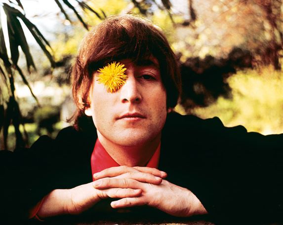 John Lennon posing with yellow flower placed over one eye