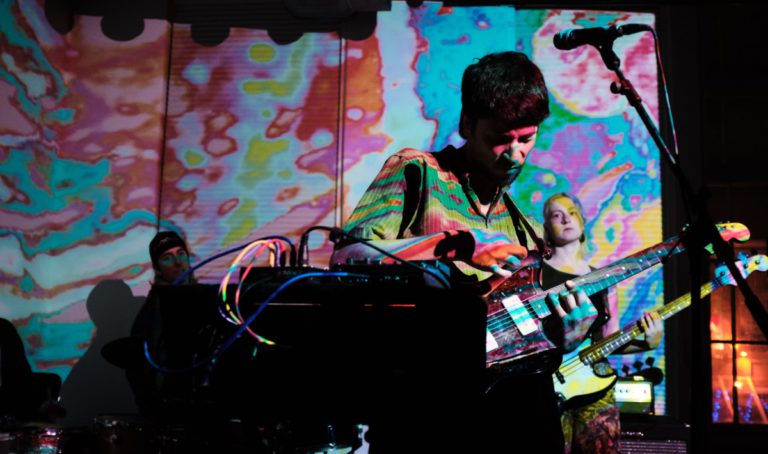 The Dead Shakers performing live with guitarist/vocalist Kevin Bloom out front and psychedelic projected on him and the backdrop
