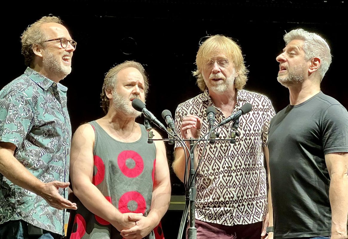The four members of Phish standing together singing a capella