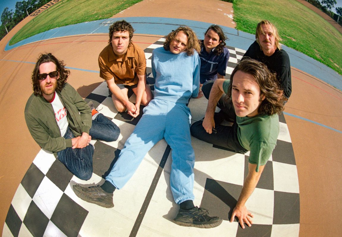 Fish-eye lens image of King Gizzard band members sitting outside on a checkerboard blanket