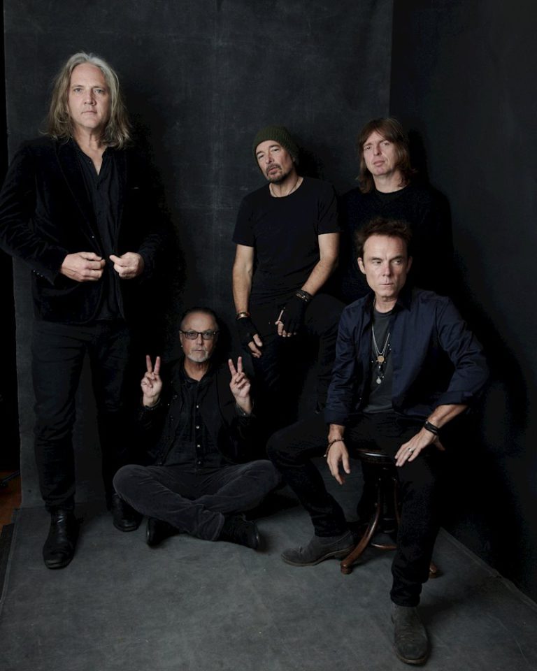 Members of the band The Church all wearing black standing in front of black backdrop