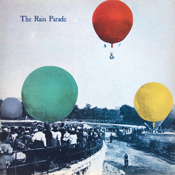 Black and white photo of crowds at a bicycle race with green, red, and yellow hot air balloons floating overhead.
