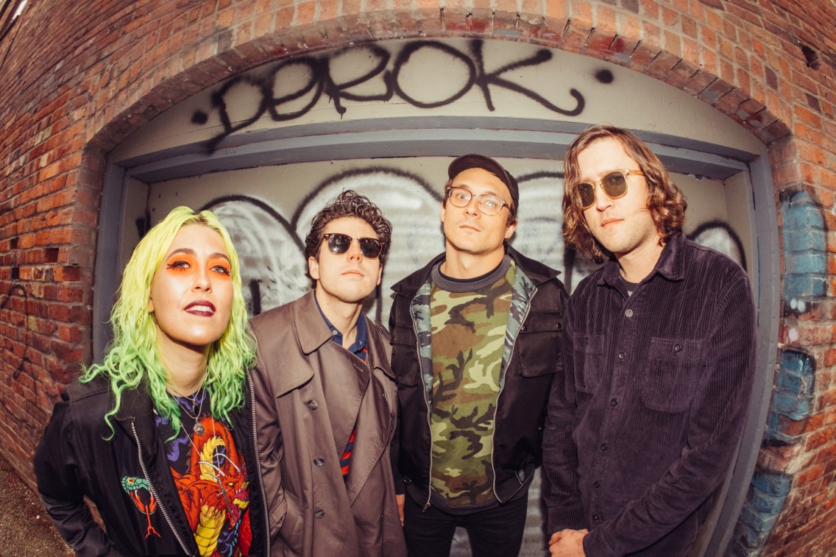 Fish-eye lens image of the four members of Frankie and the Witch Fingers standing in front of a brick wall with graffiti