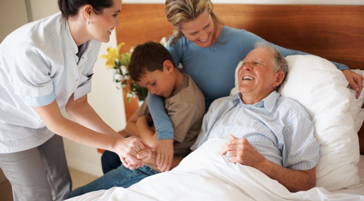 Smiling older man in hospital bed with nurse, daughter, and grandson at his side