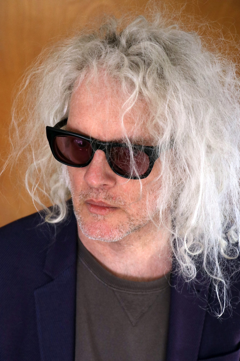 White man with long white hair and sunglasses and black t-shirt