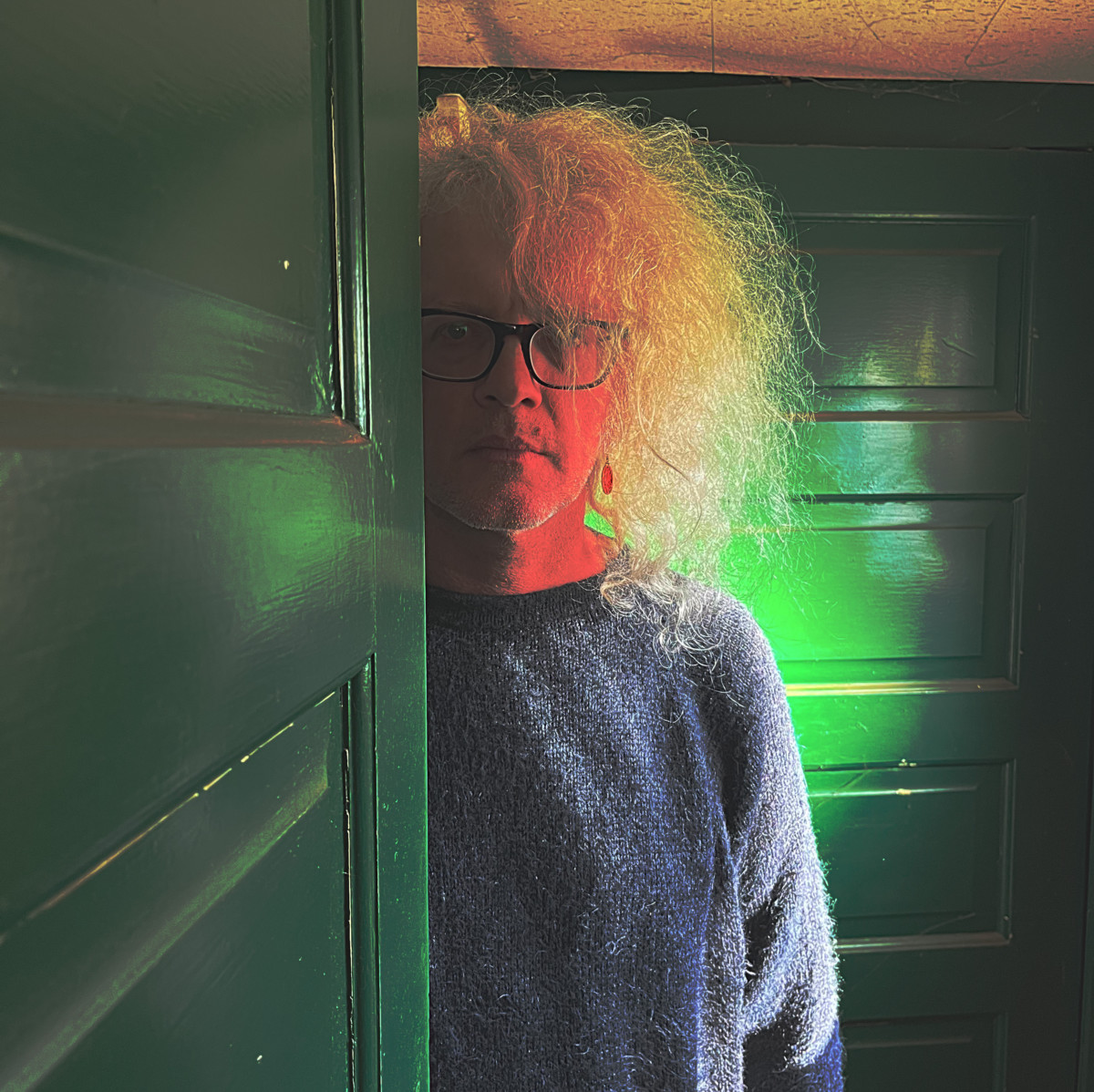 Image of Anton Barbeau standing behind open door with green background