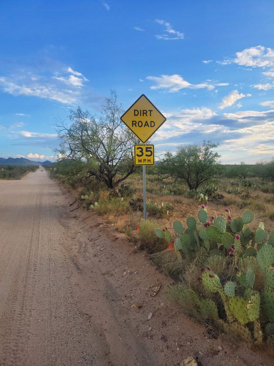 Image of a dirt road in the desert with a yellow diamond-shaped sign saying "Dirt Road" and another square sign saying "35 MPH"