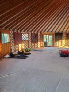 Photo showing the inside of the yurt with its geometrical ceiling and spacious floor with a couple of sleeping backs set against the interior wall