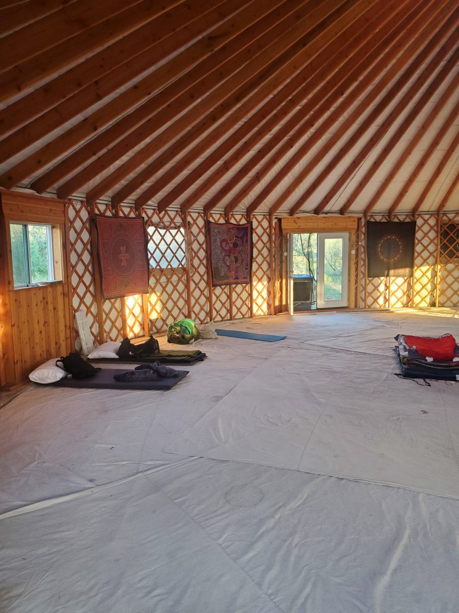 Photo showing the inside of the yurt with its geometrical ceiling and spacious floor with a couple of sleeping backs set against the interior wall