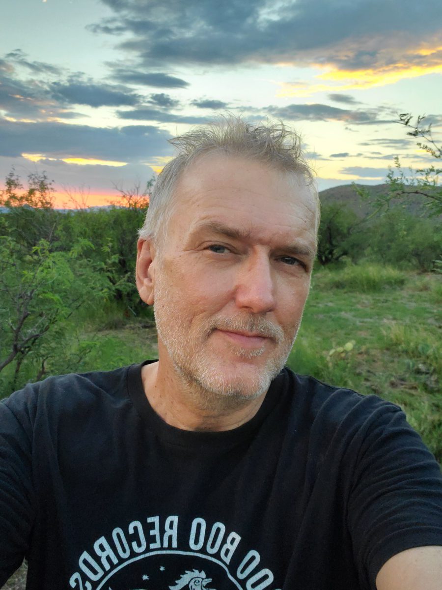 Photo of the author in black t-shirt with lush green desert and sunset behind him