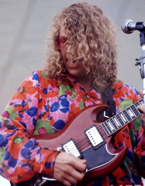 Color photo of a young Barry Melton in brightly and multi-colored shirt playing electric guitar