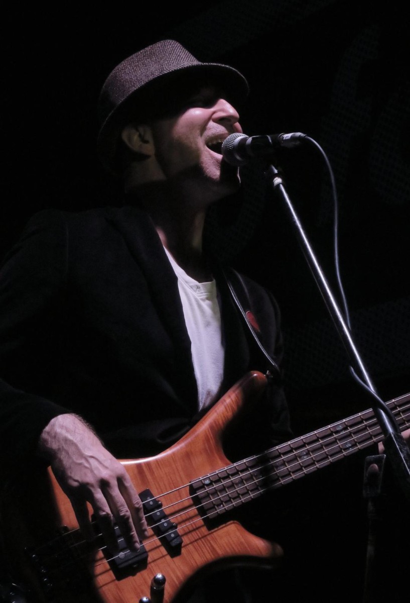 Malcolm Bruce wearing a black jacket over a white shirt playing bass and singing.
