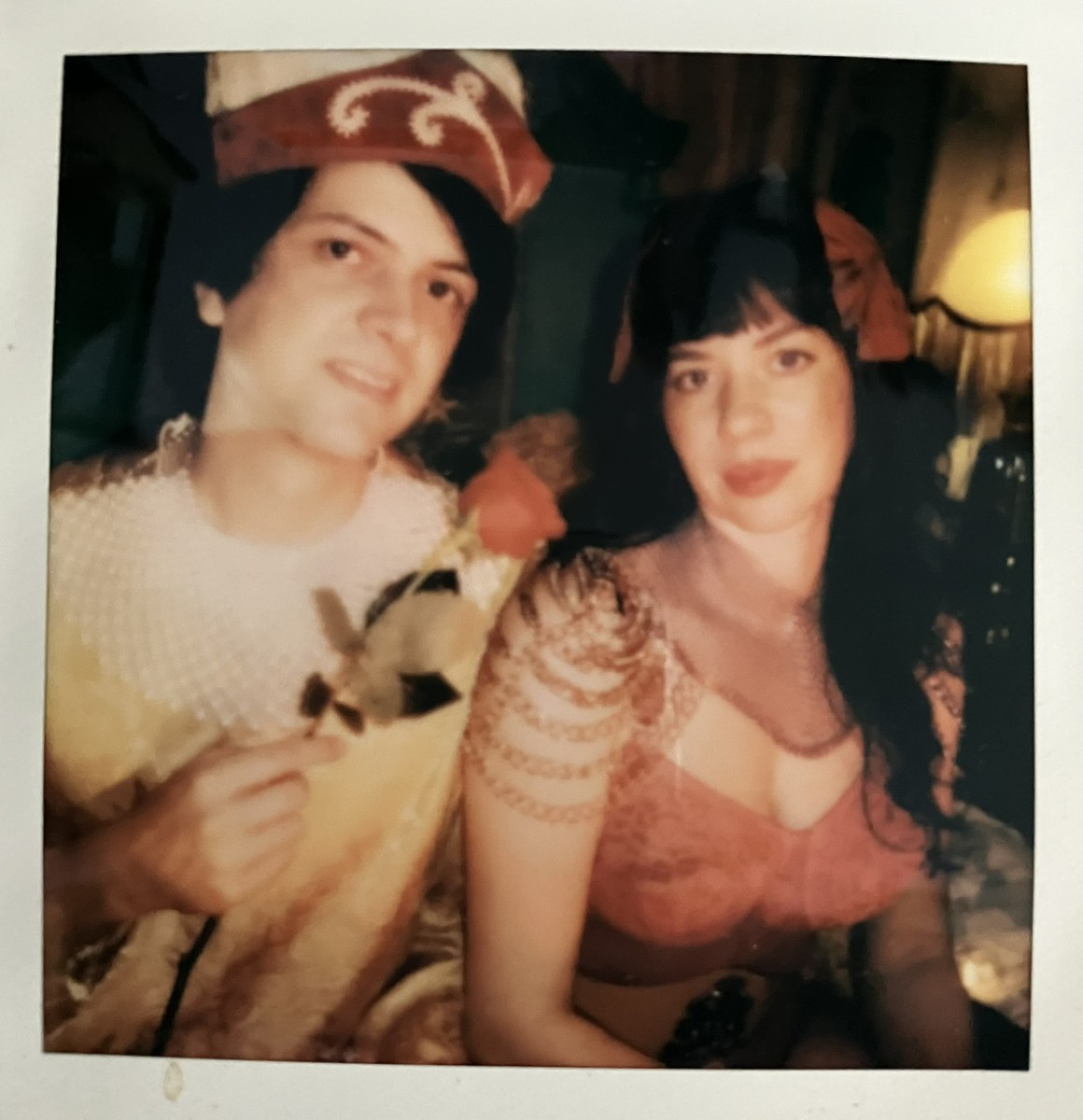 Polaroid photo of a young man wearing a crazy hat and holding a flower and a young woman with long, brown hair wearing a dress.