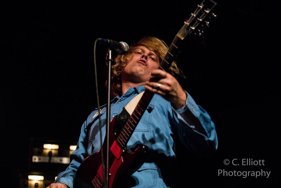 Photo looking up at Ty Segall in blue shirt as he plays guitar wildly.