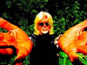 Man with long white hair and goatee weaing black shirt with hands outstretched toward the camera