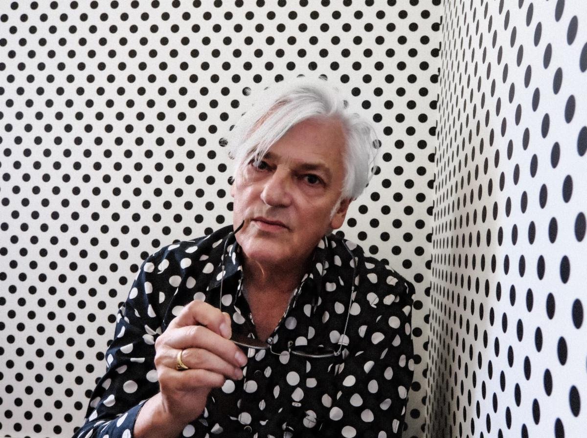 Robyn Hitchcock in black shirt with white polka dots in a room with white walls and black polka dots