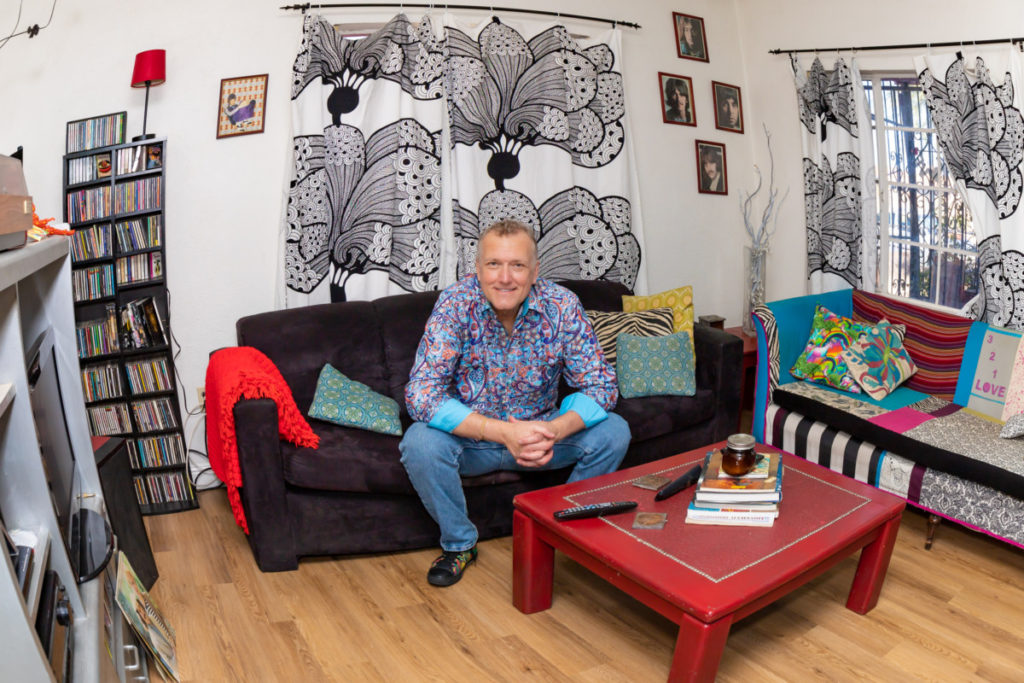 White man in colorful clothes sitting in colorful living room