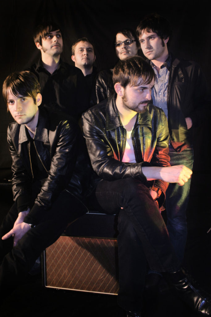 Six white men in dark clothes posting for photo with dark background