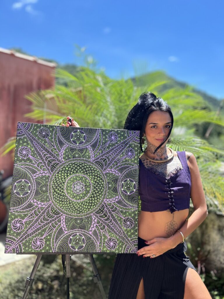 Attractive young brunette holding up piece of geometrical art with green tree and green mountain in background