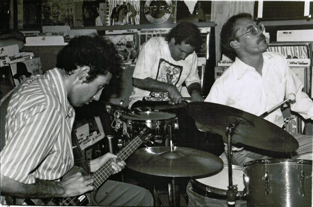 Black and white photo of the three members of Sun City Girls performing together in tight quarters.