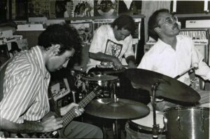 Black and white photo of the three members of Sun City Girls performing together in tight quarters.