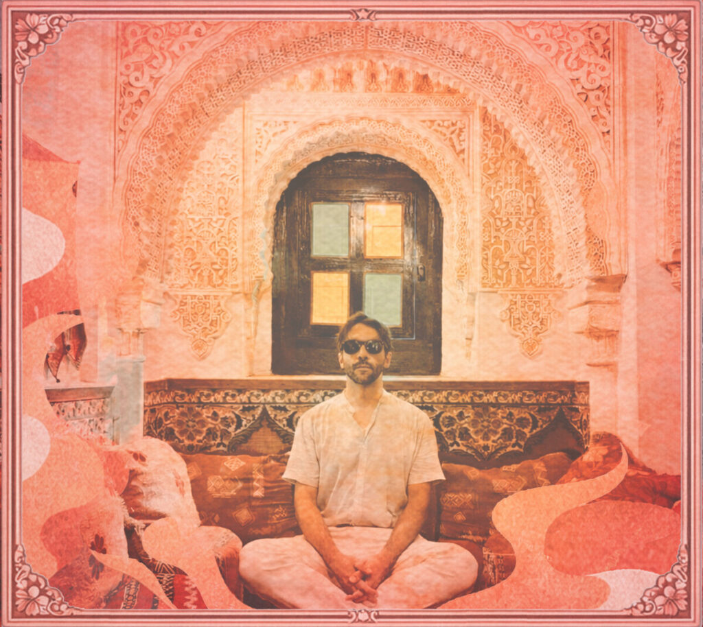 A man sitting on the floor lotus style with a pink archway behind him and pink decor all around.