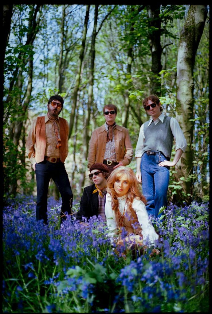 The five members of The Crystal Teardrop sitting or standing in a flowery clearing in a forest