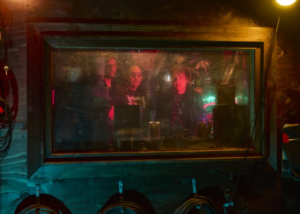 Blurry, color photo of the men from Sleep through a studio window