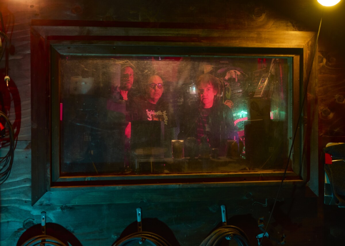 Blurry, color photo of the men from Sleep through a studio window