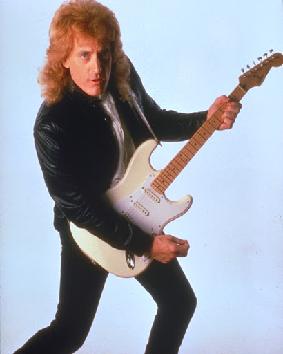 Color photo of Tommy James with guitar with 80s hairstyle and suit